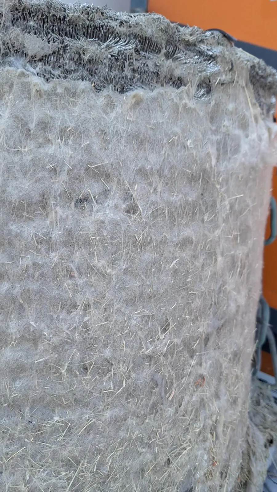 Close-up of a Utah AC condenser coil with a thick felted layer of cottonwood fluff and foxtail seeds, with the aluminum fins visible only at the torn top edge